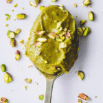 Pistachio butter in jar on wooden table with whole pistachio